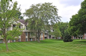A large grassy area with trees in front of an apartment complex